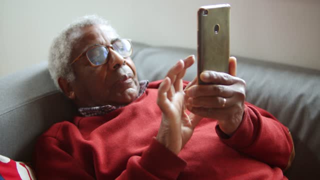 An Elderly Man Using a Cellphone on a Couch