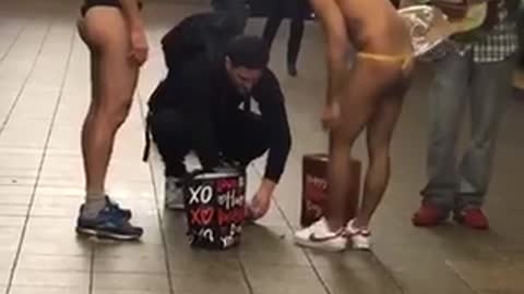 Two subway performers stand at the station only wearing thongs