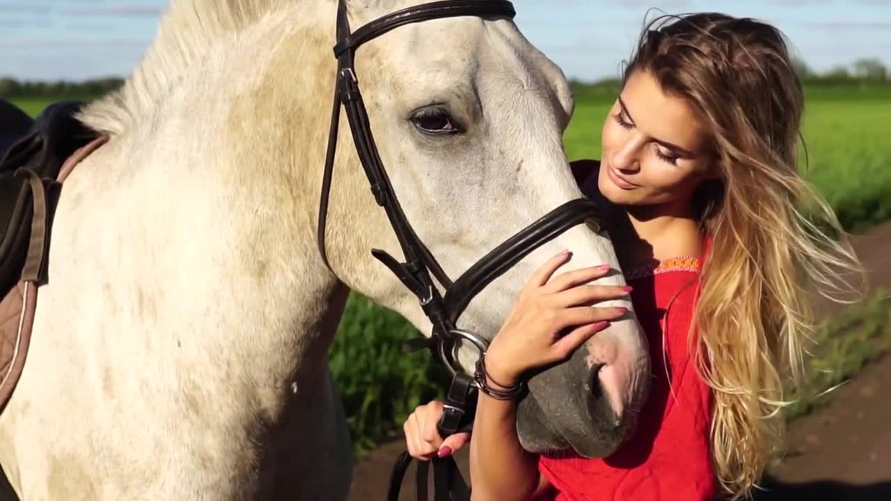 Portrait of young beautiful woman dreesed in red with white horse near the field