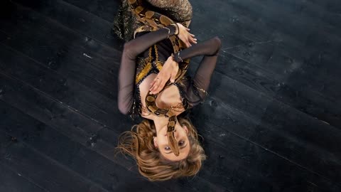 Attractive woman in bright costume dance lying on the floor with a snake