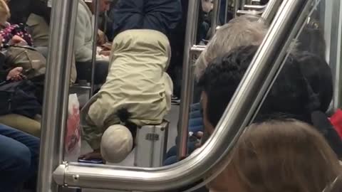 Older man in hate does hand stand on train