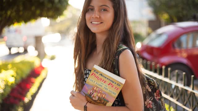 Happy Girl Walking in a Park Carrying a Book