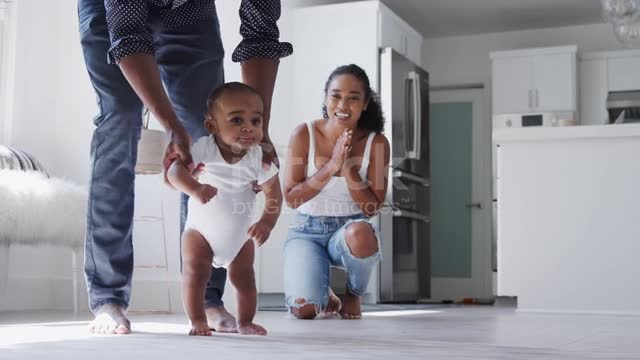 parents-encouraging-smiling-baby-son-to-take-first-steps-and-walk-at-home تشجيع الطفل على المشي