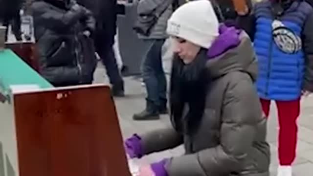 A Ukrainian woman plays the piano at a train station in Lviv while dozens around her try to leave