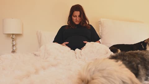 A Pregnant Woman with Her Dogs on the Bed