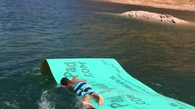 Boy slides down boat slide bellyflop on blue mat