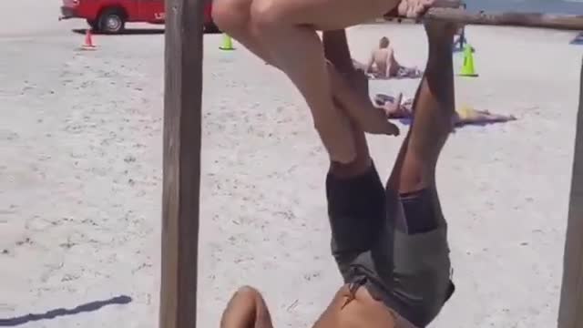 Guy Workouts At Beach While Hanging Upside Down On a Rod