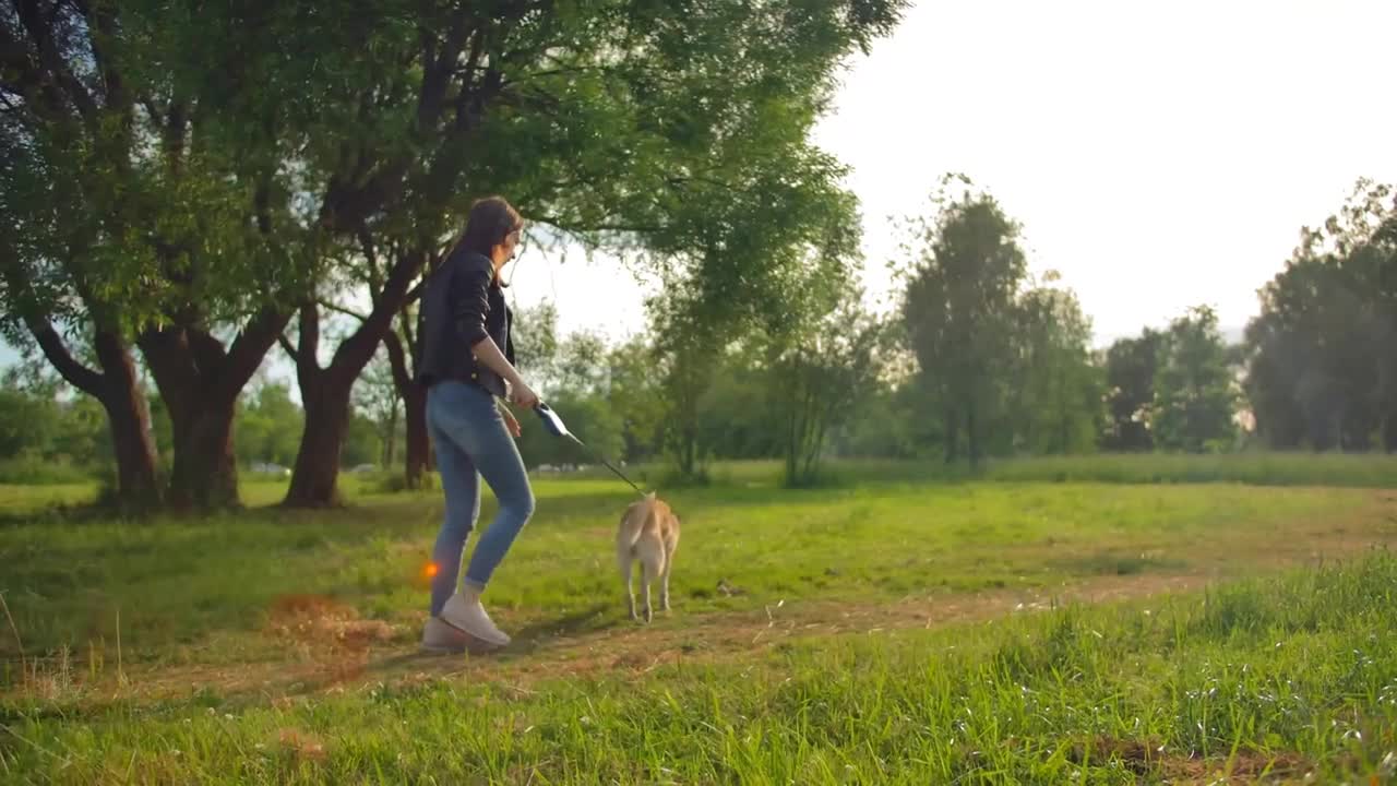 Wide profile shot of a girl, leading a dog on a leash in the park