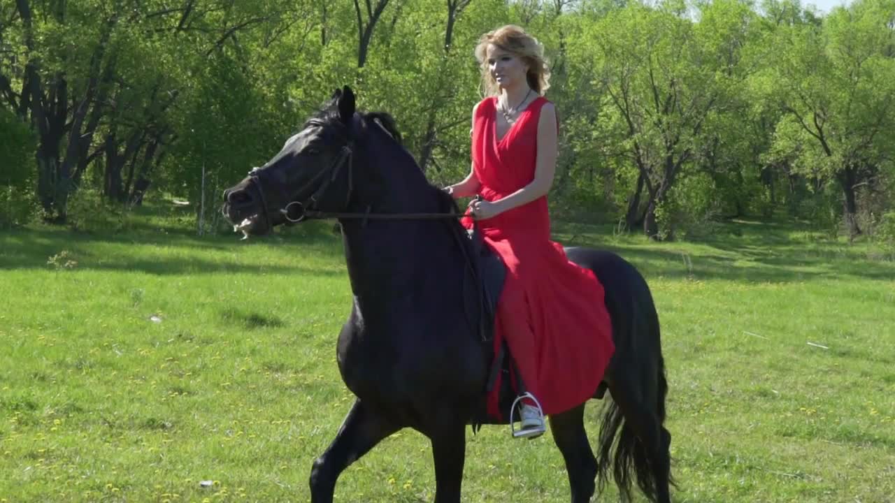 Young woman in red dress riding black horse bareback