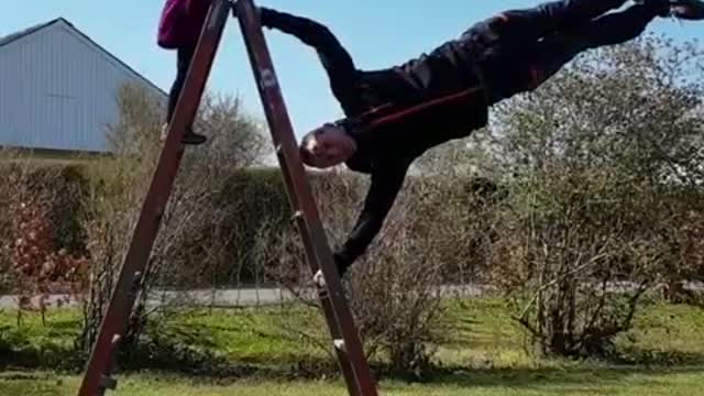 Man Performs a Flagpole Balance On Ladder While Daughter Observes Him