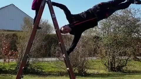 Man Performs a Flagpole Balance On Ladder While Daughter Observes Him