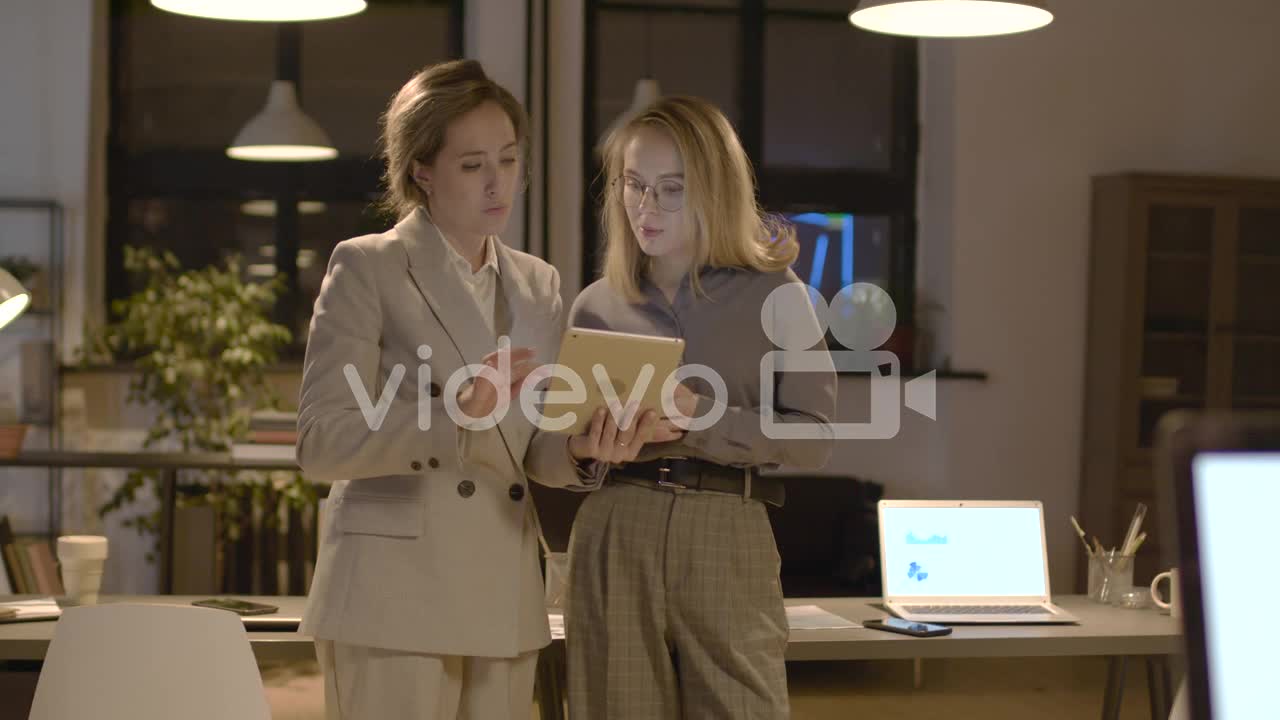 Two Female Coworkers Talking And Watching A Tablet Standing In The Office 2