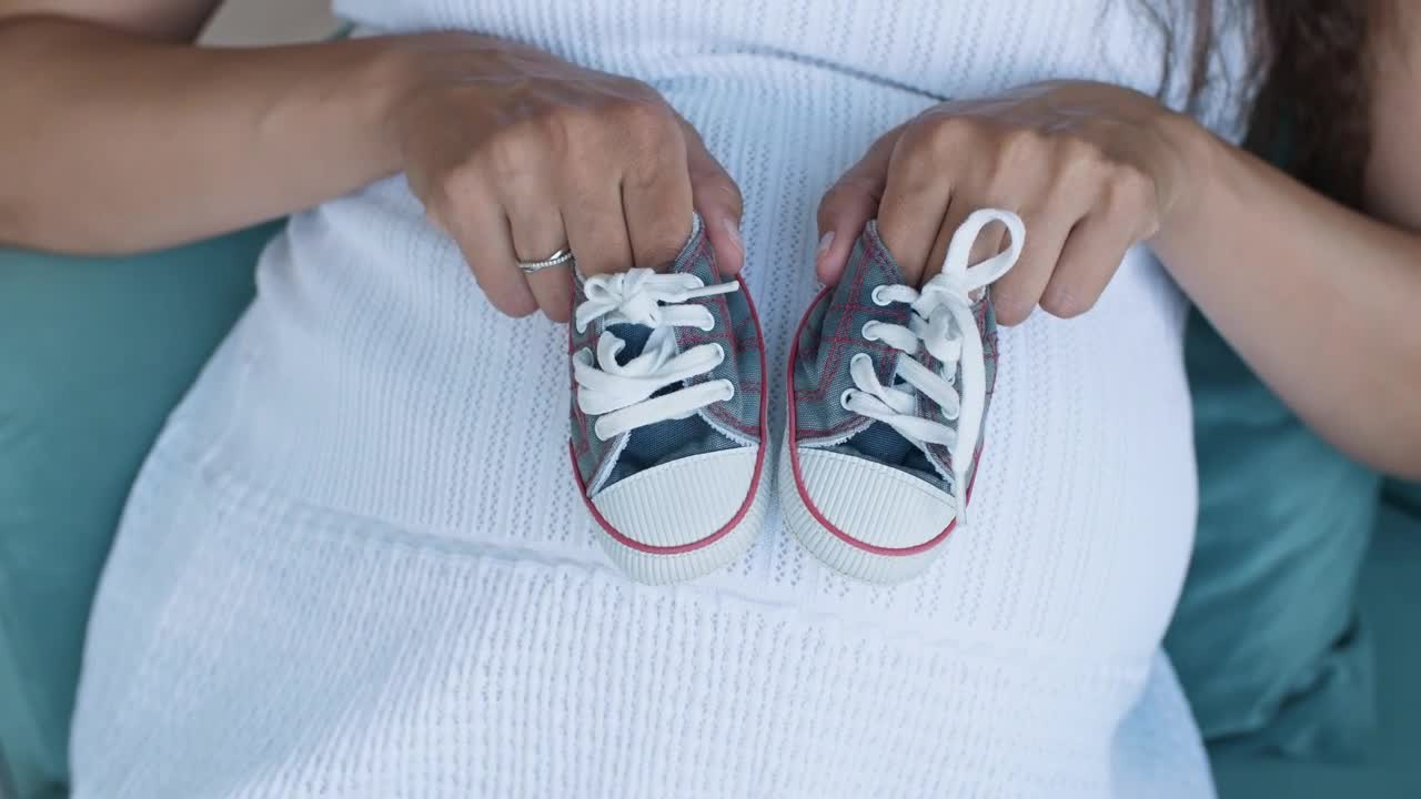 Pregnant woman holding small baby shoes, top shot