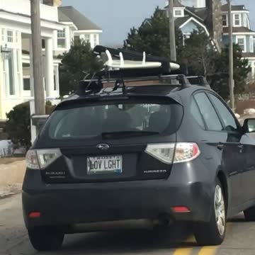 Black car drives off with white surfboard on roof