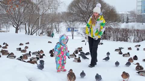A mother and daughter dressed in bright warm jackets are feeding birds