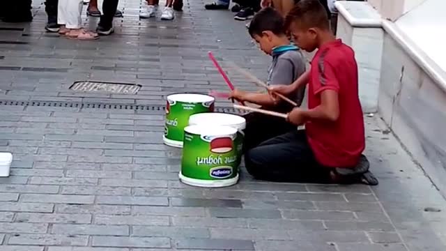 Two Boys Playing Drums Out Of Plastic Buckets