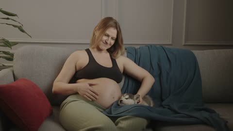 A pregnant woman spends an evening with a pet. They are sitting on the couch
