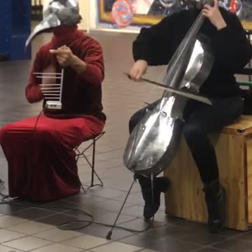 Silver skull and silver bird helmet playing cello violin in subway red dress black suit