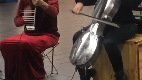 Silver skull and silver bird helmet playing cello violin in subway red dress black suit