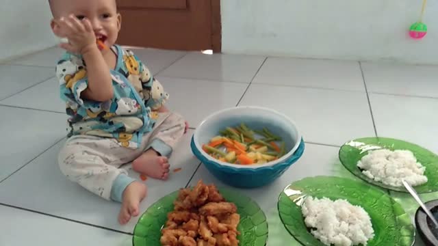 Indonesian baby happily eating vegetables by himself