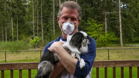 Mature adult male wearing a mask while holding his Japanese Chin dog; COVID-19 and pets theme