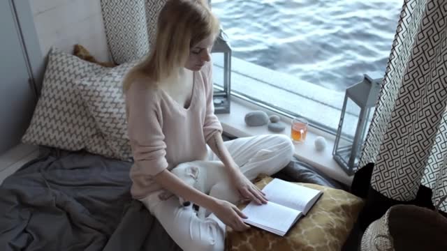 girl with a puppy reading a book sitting by the window with a lake view