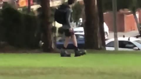 Guy with backpack on rollerblades walks on grass