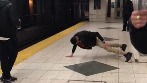 Khaki pants black jacket one armed pushups subway platform