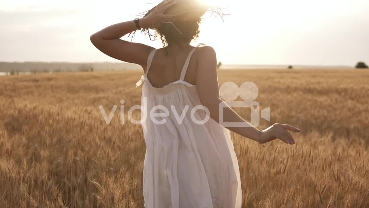 Young Woman Running In The Wheat Field While Holding Her Straw Hat