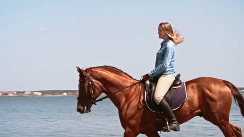 Tracking of elegant smiling woman with her hair flying wildly galloping on her horse along lake