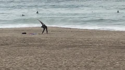 Guy uses surfboard to stretch on the beach