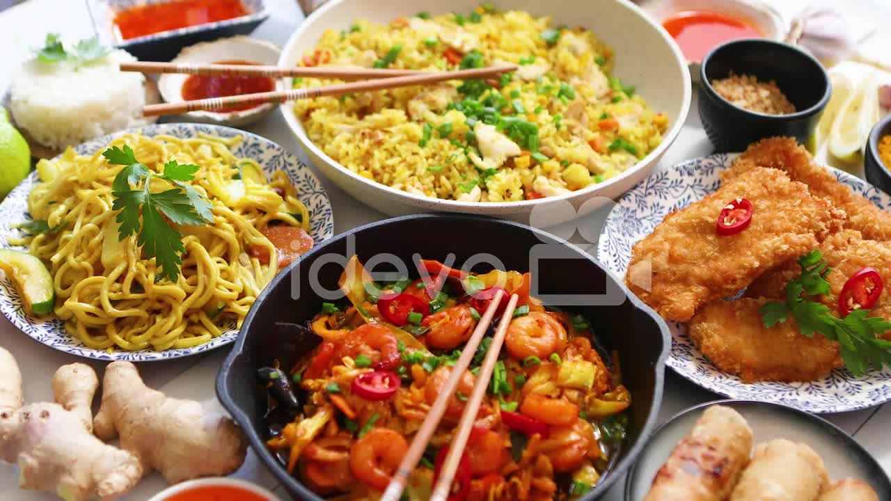 Asian food served Plates pans and bowls full of noodles chicken stir fry and vegetables