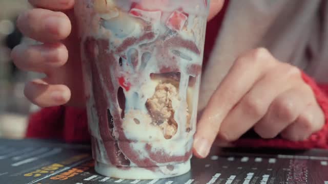 A girl turning a plastic cup filled with chocolate ice cream_batch