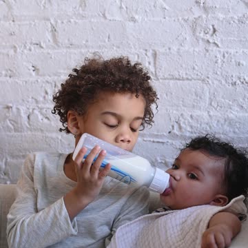 The elder brother is giving milk to the younger brother.