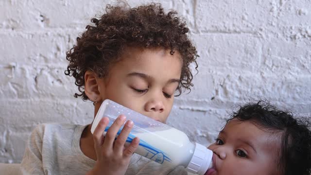 The elder brother is giving milk to the younger brother.