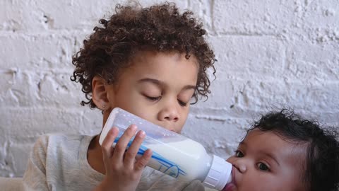 The elder brother is giving milk to the younger brother.