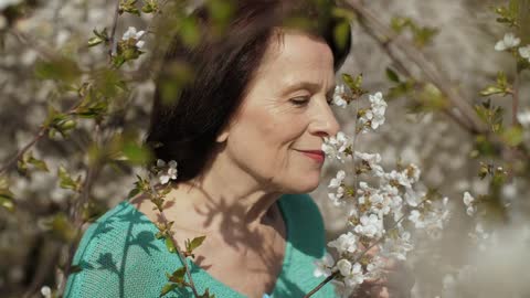 Old woman smelling flowers from her garden