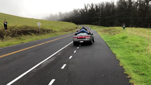 A Daredevil Holds On The Roof Of A Moving Car