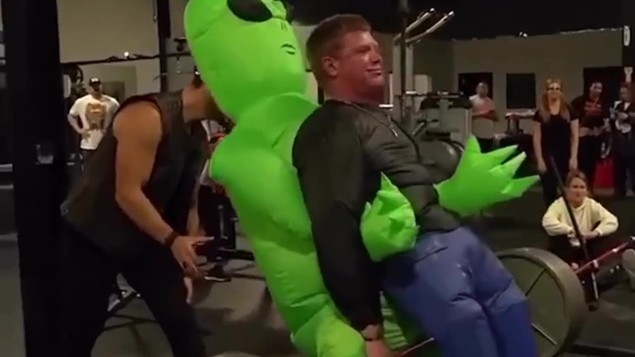 An alien does a barbell lift with a human