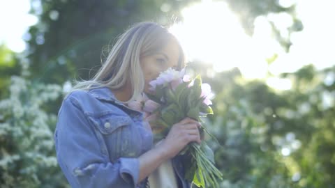 Woman in denim jacket smelling flowers on spring day