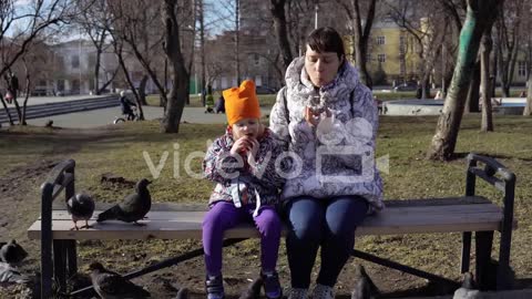 A young woman and a little girl eat buns and feed pigeons on a cold, cloudy day