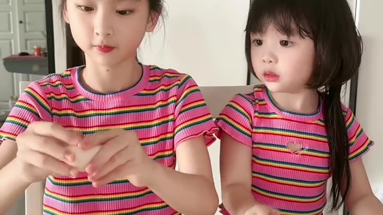 Two little girls are breaking eggs by touching them with their foreheads.