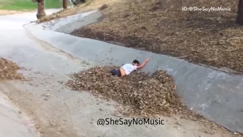 White shirt skateboards into leaf pile drainage ditch