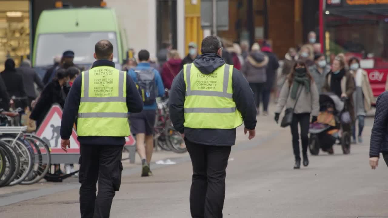 Long Shot of Public Service Workers Walking Down a Busy Street In Oxford England