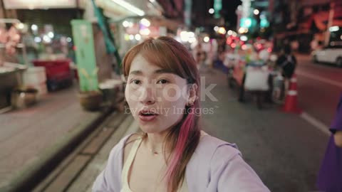 Young woman filming a vlog selfie in the night market at thailand