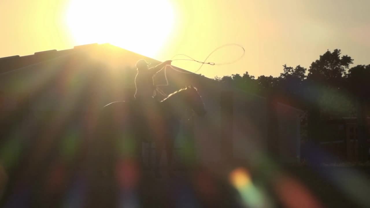 Boy on horse swinging lasso in sunset slow motion