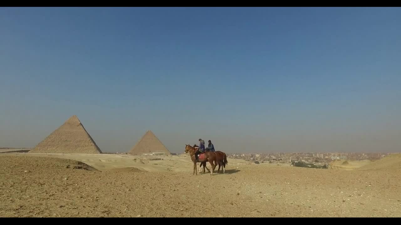 Woman riding horse with local man in front of Giza pyramids, Egypt