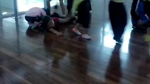 Little girls holding onto each others neon green shirts one girl in red falls and hits floor