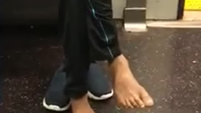 Man in blue sweater barefoot sitting in subway seat