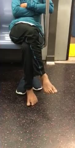 Man in blue sweater barefoot sitting in subway seat
